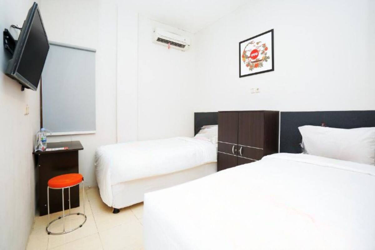 A hotel room with two beds, a desk, a chair, a TV, and an air conditioning unit.