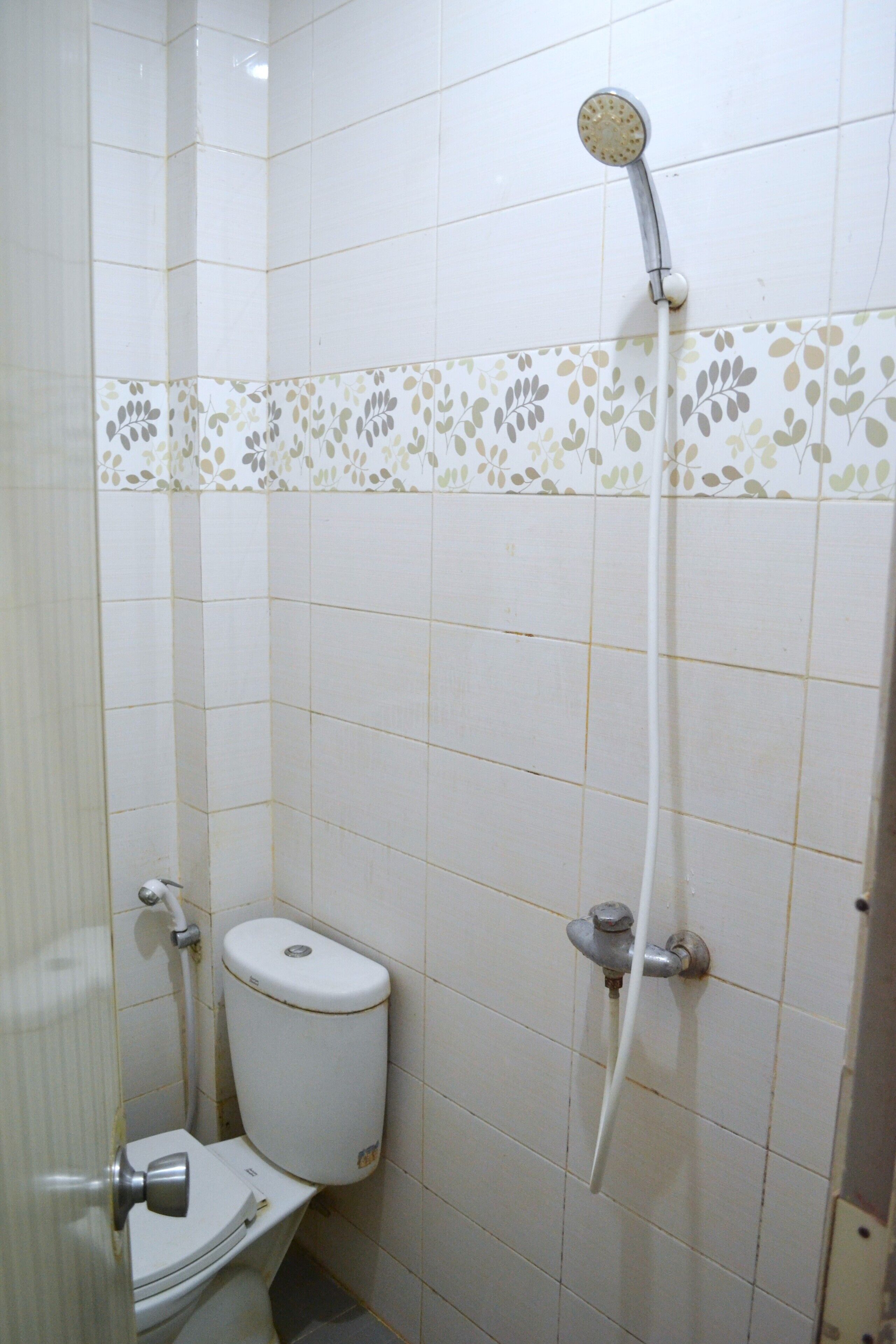 A small bathroom with a toilet, a shower, and a wall with a floral tile border.