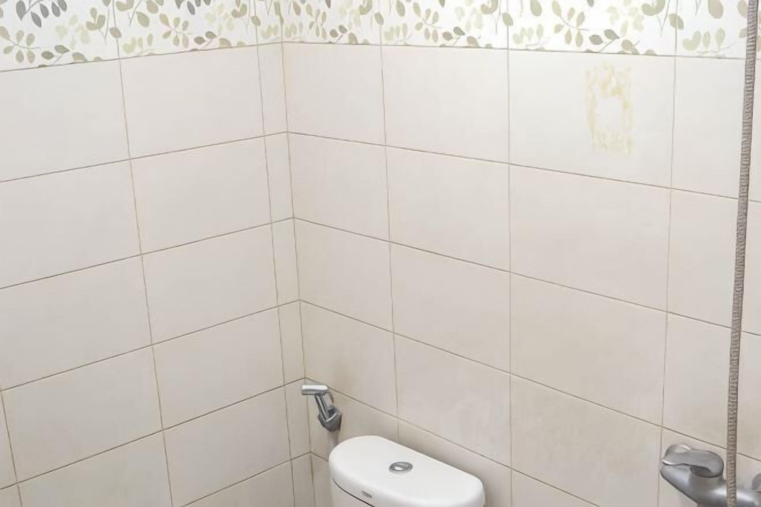 A bathroom with white tiles, a toilet, and a shower area.