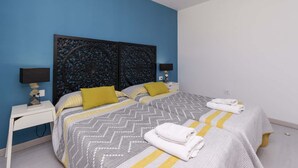 Una habitación de hotel con dos camas, un ventilador de techo y una mesita de noche con lámpara.