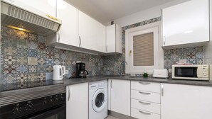 Una cocina compacta con armarios blancos, lavadora, estufa, microondas y cafetera.