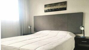 A neatly made bed with a white duvet, a grey headboard, and two bedside tables with lamps.