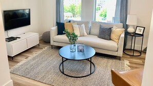 A modern living room with a sofa, a coffee table, a TV, and a window with curtains. - Spacious Designer Apartment Downtown Tulsa-Gym Access (Tulsa)