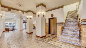 A spacious lobby with a patterned floor, a staircase with decorative tiles, and a central column with lights. - Spacious Designer Apartment Downtown Tulsa-Gym Access (Tulsa)
