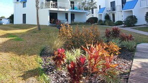A modern multi-story building with balconies, surrounded by landscaped gardens and palm trees. - Ground floor unit! Close to pool and beach. (Saint George Island)
