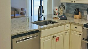 A compact kitchen with a built-in dishwasher, a sink, and a countertop with a knife block. - Ground floor unit! Close to pool and beach. (Saint George Island)