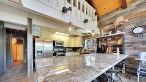 A modern kitchen with a large granite countertop, stainless steel appliances, and a wooden ceiling. - Tranquil Hillside Home w/ Private Hot Tub! (Pioneer)