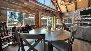 A rustic wooden interior with a round dining table, wooden chairs, and a stone fireplace. - Tranquil Hillside Home w/ Private Hot Tub! (Pioneer)