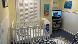 Una habitación infantil con una cuna, un televisor y obras de arte en las paredes.
