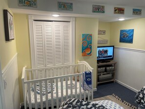 A baby room with a crib, a television, and artwork on the walls.