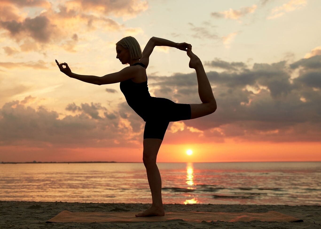 A person performing a yoga pose on a beach at sunset.