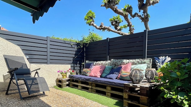 A patio with a black metal chair, a wooden bench with cushions, and decorative mushroom planters.