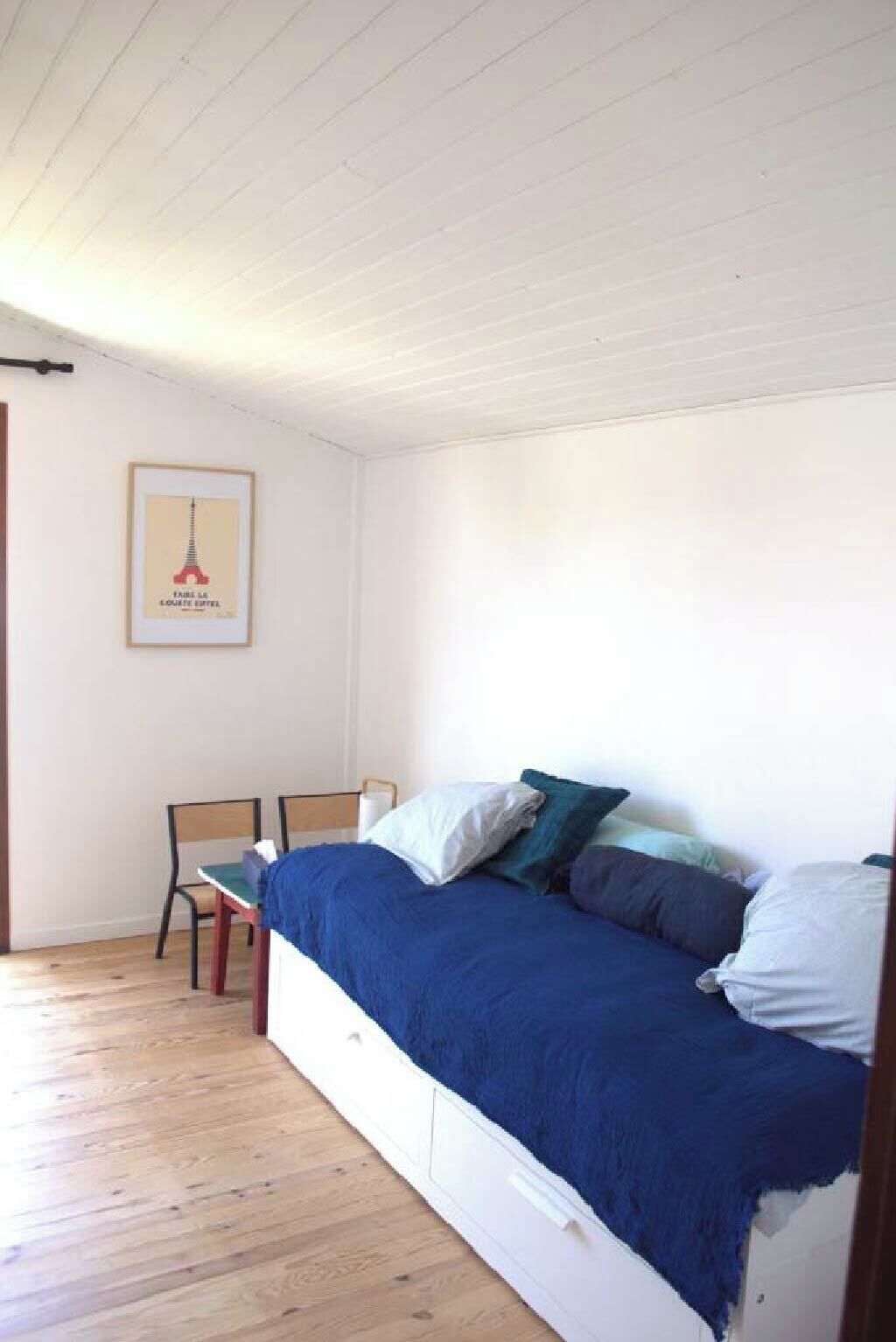 Un dormitorio con cama, dos sillas, un cuadro enmarcado en la pared y suelo de madera.