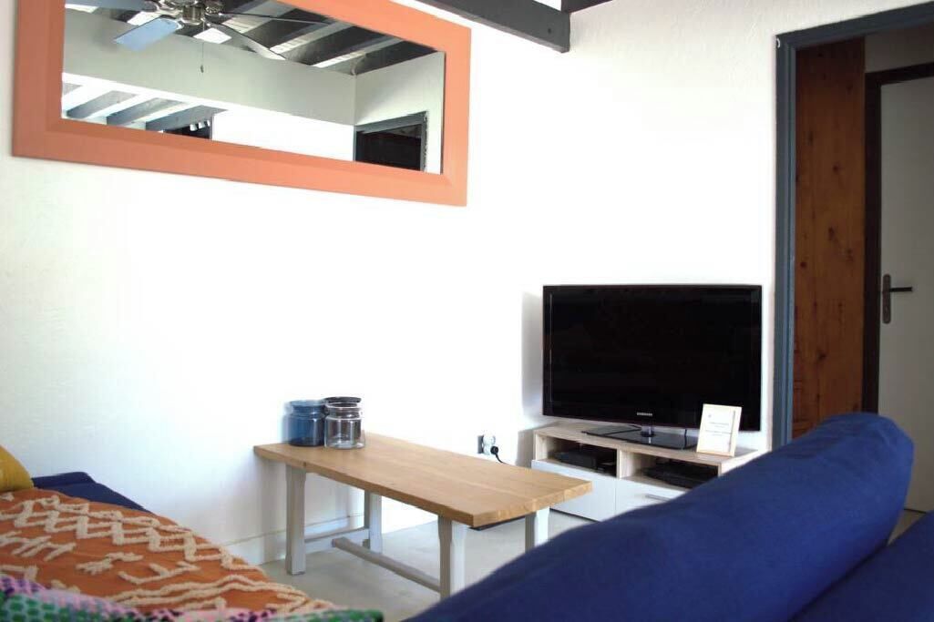 Um quarto com cama, televisão em um suporte, uma mesa de madeira e um espelho na parede.