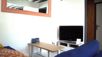 Um quarto com cama, televisão em um suporte, uma mesa de madeira e um espelho na parede.