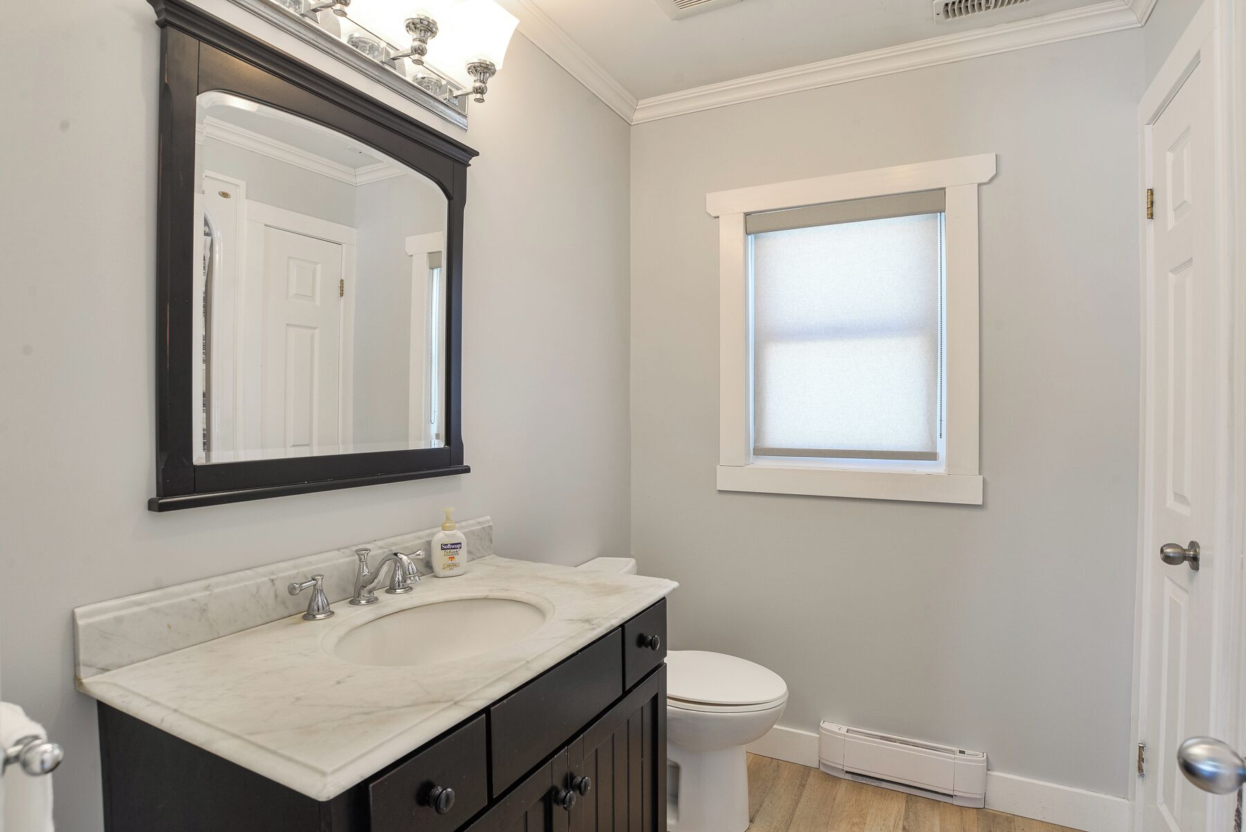 A bathroom with a white sink, dark vanity, a mirror, a toilet, and a window with frosted glass.