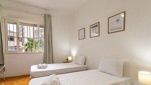 Ein Hotelzimmer mit zwei Betten, einem Fenster mit Vorhängen, einem Nachttisch mit Lampe und gerahmten Bildern an der Wand.