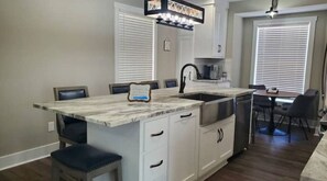 Una cucina con piano di lavoro in marmo, mobili bianchi, rubinetto nero e zona pranzo con tavolo e sedie.