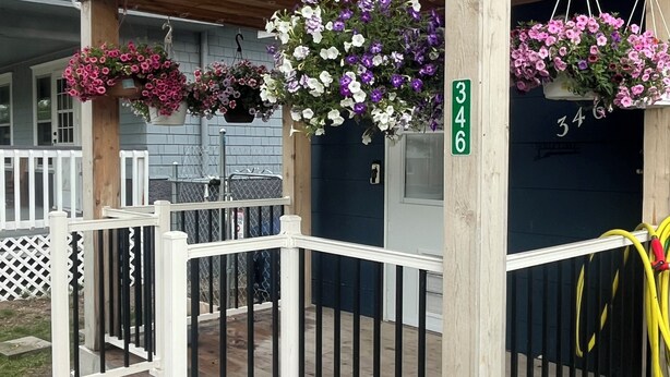 A wooden porch with a white railing, a mailbox, and hanging flower baskets. - Room in house (Lake Andes)