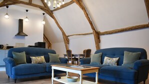 Uma sala de estar aconchegante com dois sofás azuis, uma mesa de centro de madeira e uma área de cozinha ao fundo.