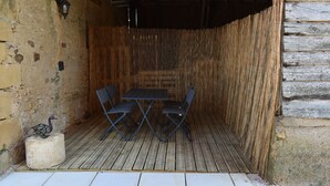 Um pátio externo com mesa e cadeiras de madeira, uma escultura decorativa de pássaro e uma parede texturizada.