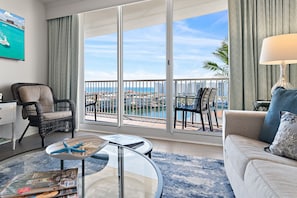 A spacious living room with a balcony overlooking a cityscape and water. - Incredible Ocean Views & Beach - The Heart of Destin Action - Walk to the Beach (Destin)