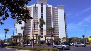 A multi-story hotel with a central entrance, surrounded by palm trees and parked cars.