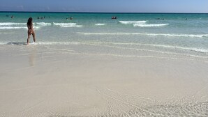 A beach with clear turquoise water, a sandy shore, and people swimming and walking.