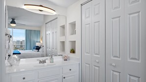 A modern bathroom with a large mirror, white cabinetry, and a ceiling fan.