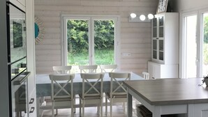 A kitchen with white cabinetry, a dining table with chairs, and a view of greenery outside. - Ecolodge Plain Pied Avec Terrasses Multiples, 8 Personnes (Fontaine-lès-Luxeuil)