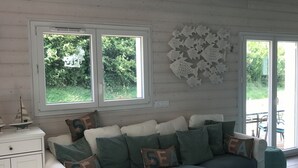 A cozy living room with a sofa, a small table, and a cabinet. There are two windows with a view of greenery outside. - Ecolodge Plain Pied Avec Terrasses Multiples, 8 Personnes (Fontaine-lès-Luxeuil)