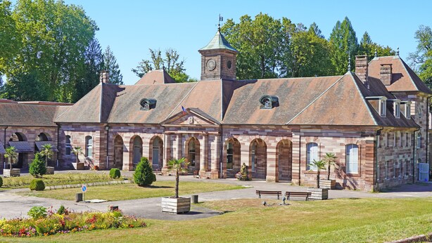A historic building with a central tower, arched windows, and a courtyard with benches and potted plants. - Ecolodge Plain Pied Avec Terrasses Multiples, 8 Personnes (Fontaine-lès-Luxeuil)