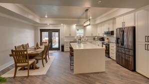 Una cocina moderna con armarios blancos, una isla central, electrodomésticos de acero inoxidable y un comedor con sillas y mesa de madera.