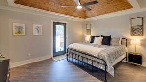 Un dormitorio con techo de madera, cama con estructura metálica, mesita de noche con lámpara y obras de arte enmarcadas en las paredes.