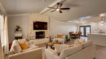 A spacious living area with a fireplace, comfortable seating, a dining area, and a kitchen.
