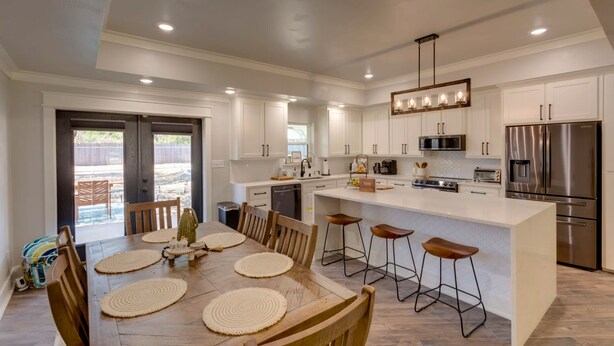 Una cocina moderna con armarios blancos, electrodomésticos de acero inoxidable y una isla central con taburetes de bar.