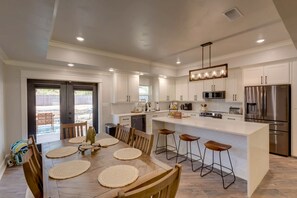 Una cocina moderna con armarios blancos, electrodomésticos de acero inoxidable y una isla central con taburetes de bar.