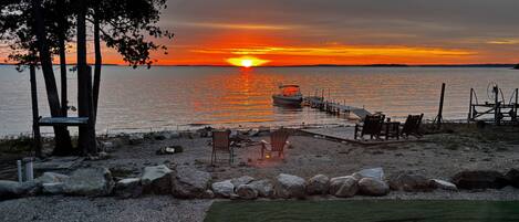 A sunset view over a calm body of water with a dock extending into the water, surrounded by rocks and a grassy area with seating.