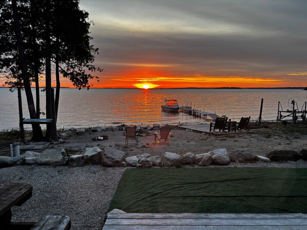 A sunset view over a calm body of water with a dock extending into the water, surrounded by rocks and a grassy area with seating.