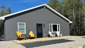 A gray single-story house with a covered porch, two Adirondack chairs, and a small table. - Beautiful, waterfront home located on the St Mary’s River, fisherman’s dream  (De Tour Village)