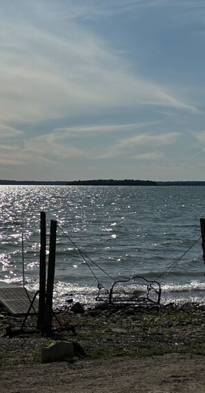 A beach with a metal swing chair and a chain fence. - Beautiful, waterfront home located on the St Mary’s River, fisherman’s dream (De Tour Village)
