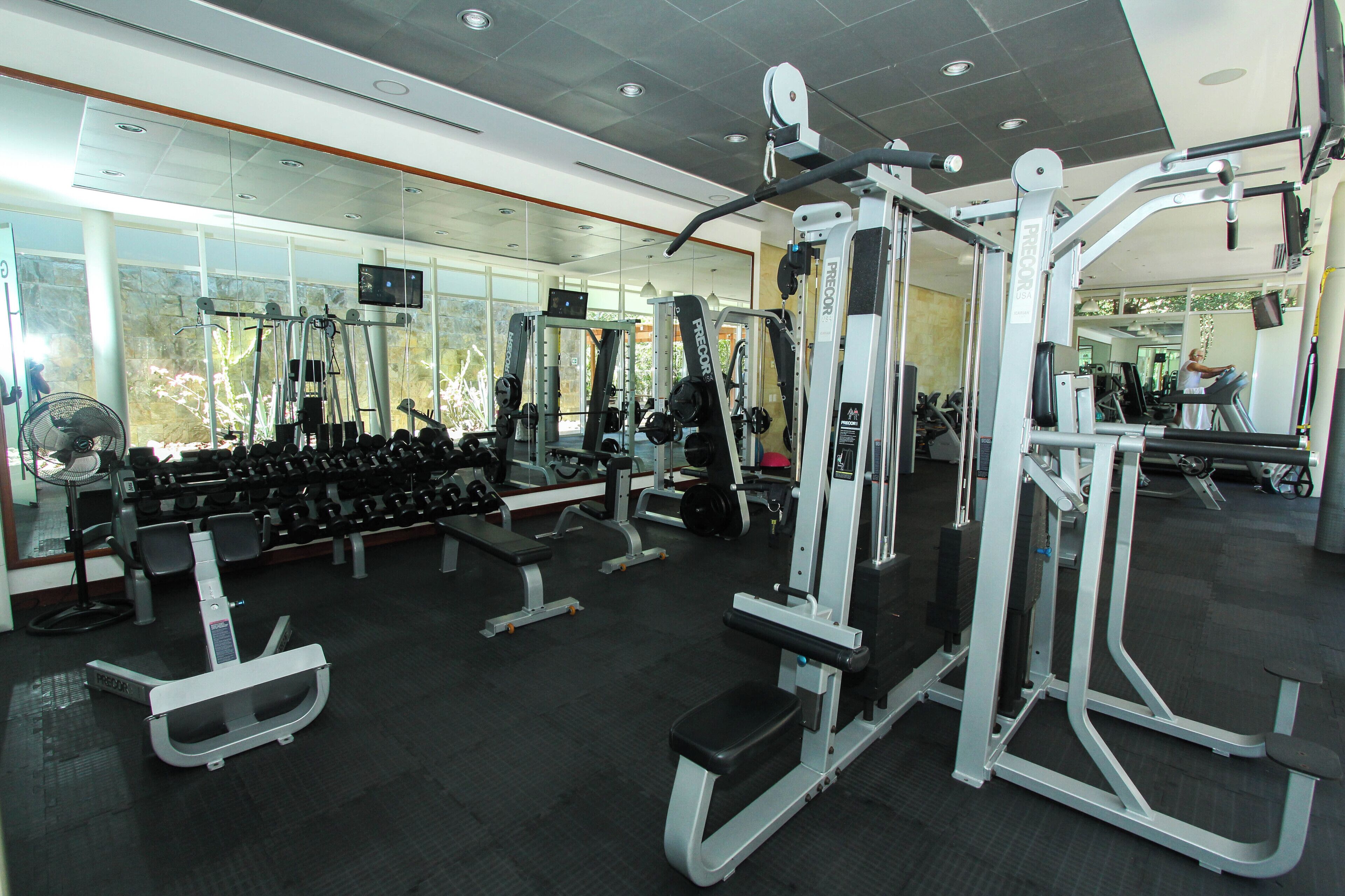 Un gimnasio con diferentes máquinas de ejercicio, pesas y un espejo grande.