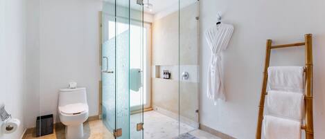 A modern bathroom with a glass shower enclosure, a toilet, a wooden ladder with towels, and a white robe hanging on the wall.