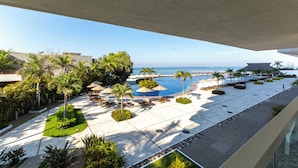 A resort pool area with palm trees, lounge chairs, and a view of the ocean. - Capitalia Tres Mares Beach Residences & Marina (Puerto Vallarta)