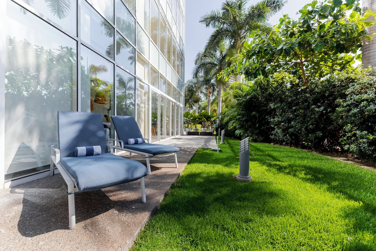 A modern outdoor seating area with two lounge chairs and a small table, surrounded by lush greenery and a well-maintained lawn.
