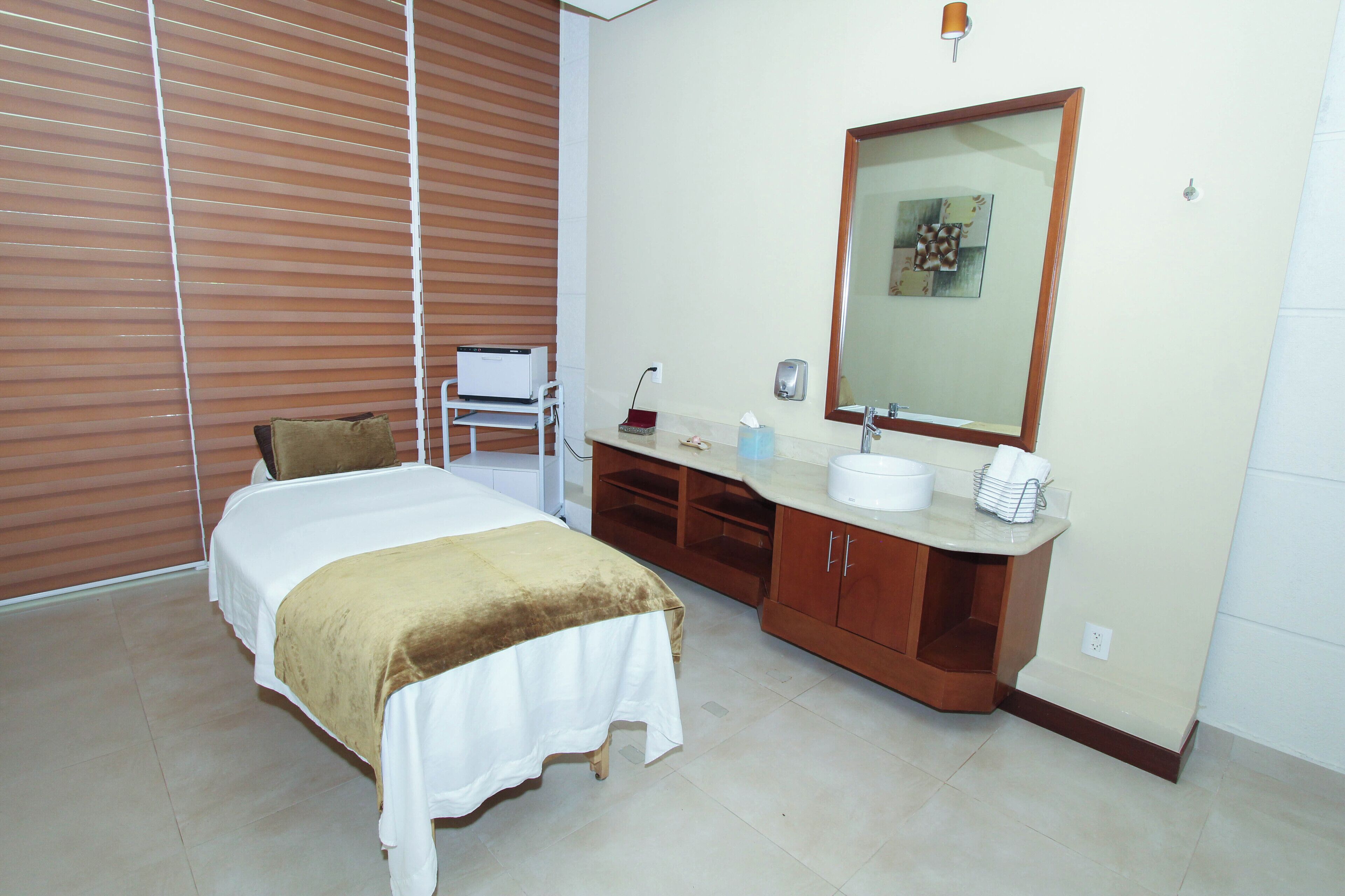A hotel room with a bed, a bathroom with a sink and mirror, and a window with blinds.
