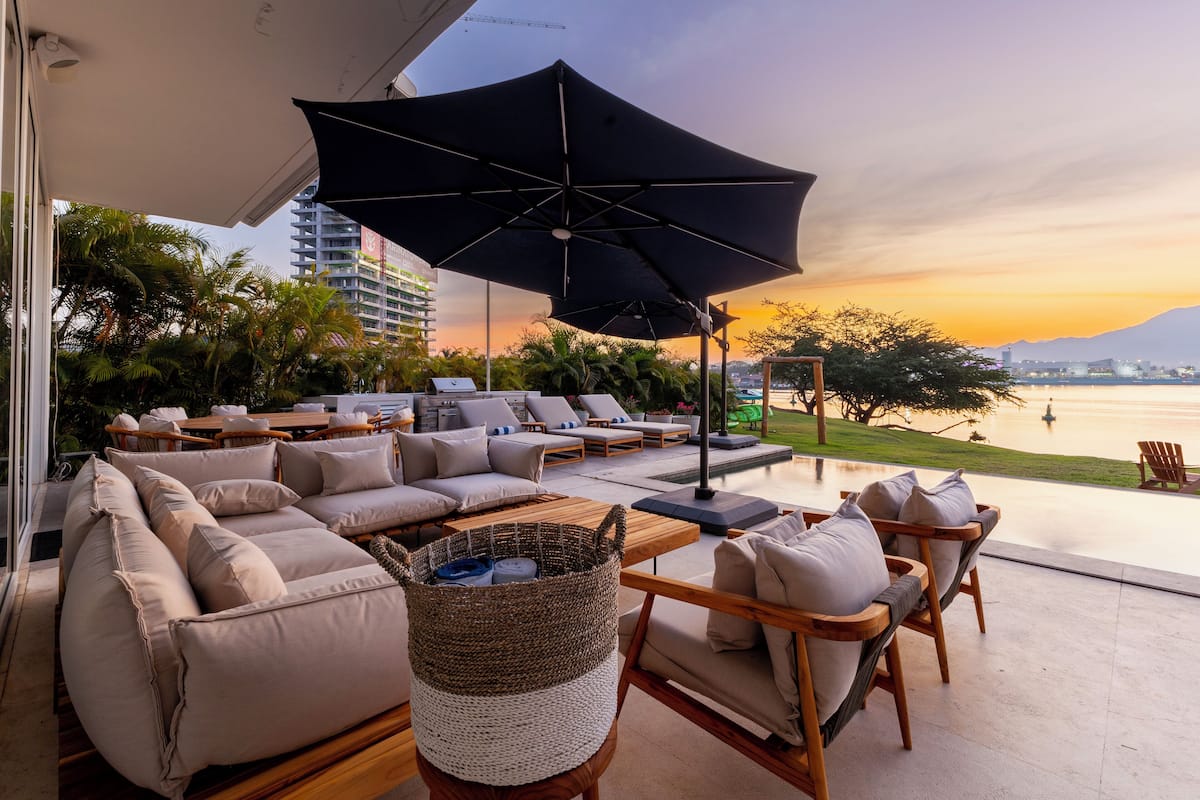 A modern outdoor lounge area with a sofa, chairs, and a large umbrella.