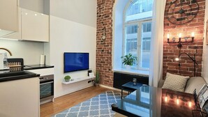Eine moderne Küche mit weißen Schränken, einer schwarzen Arbeitsplatte und einem integrierten Fernseher. Es gibt eine Ziegelwand, ein großes Fenster mit Blick und einen kleinen Tisch mit einer Pflanze.