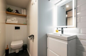Casa de banho moderna com sanita, lavatório com espelho e prateleiras com toalhas e produtos de higiene pessoal.