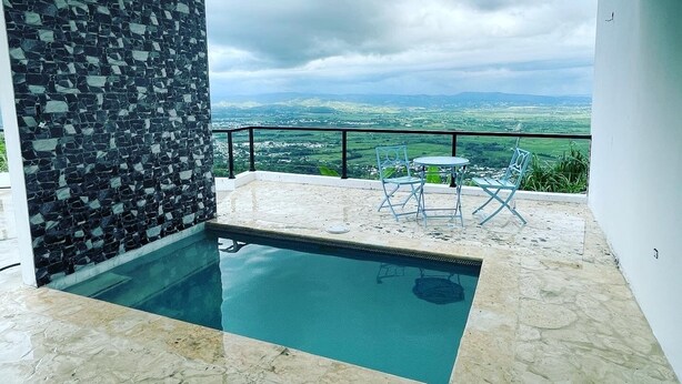 A modern outdoor pool area with a stone wall and a view of the countryside.